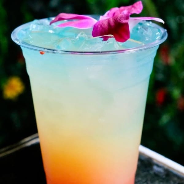 A vibrant, layered cocktail with blue, yellow, and orange hues, garnished with a pink orchid.