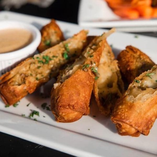 Golden-brown egg rolls with a creamy filling and green herbs, served with a dipping sauce.
