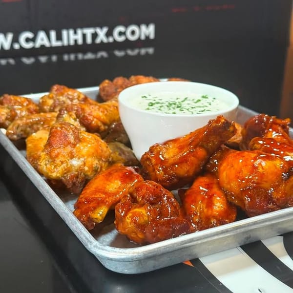 A tray of Cali Kitchen and Bar's chicken wings, some sauced, with a side of ranch.