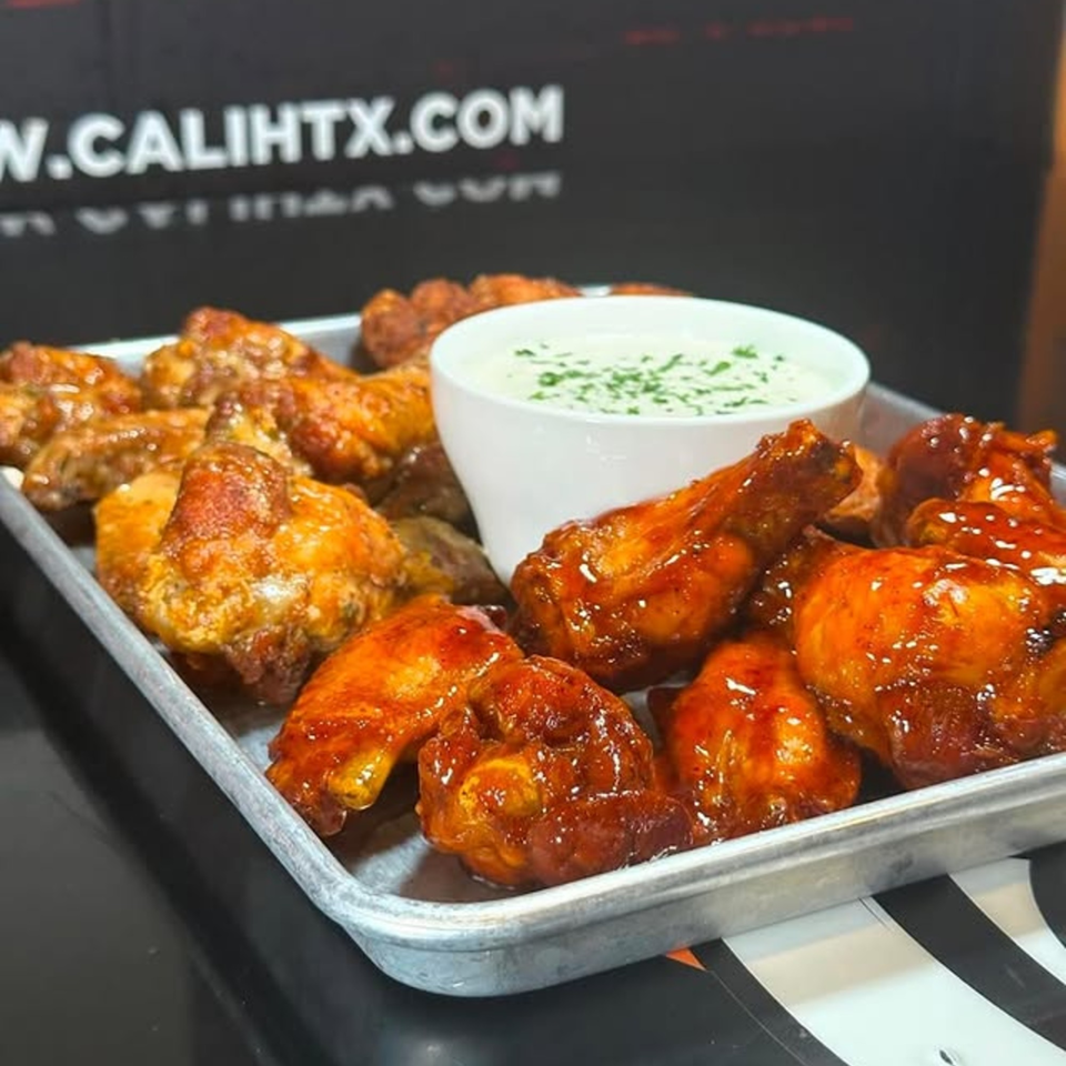 A tray of Cali Kitchen and Bar's chicken wings, some sauced, with a side of ranch.