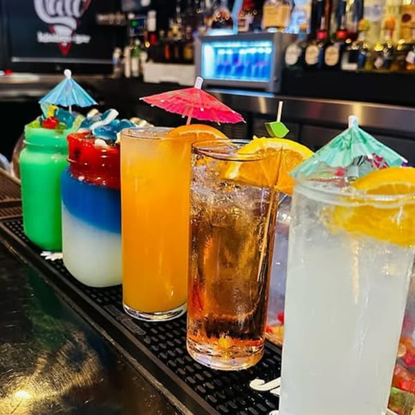 Colorful cocktails with fruit garnishes and umbrellas line a bar counter at Cali Kitchen and Bar.