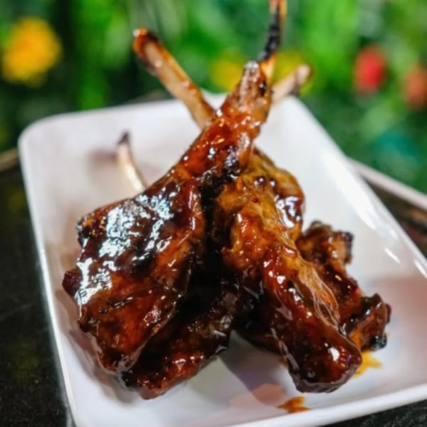 Sticky, glazed Cali Kitchen and Bar ribs on a white plate with a green background.