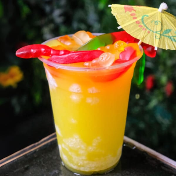 A vibrant yellow and orange drink with gummy candies and a small yellow umbrella.