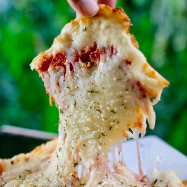 Hand pulling a slice of cheesy pizza with melted cheese strings against a green background.