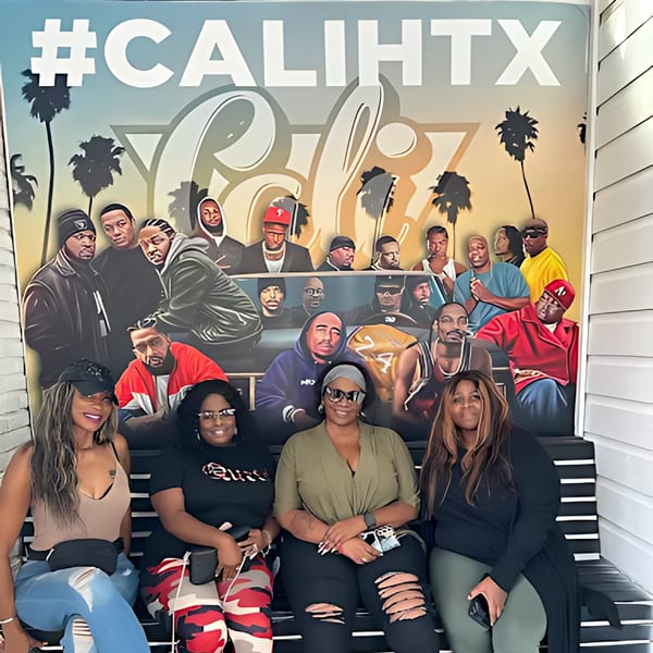 Four women smiling, sitting on a bench in front of a Cali Kitchen and Bar mural.