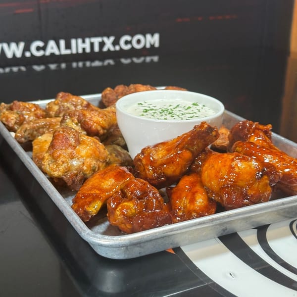 A metal tray of Cali Kitchen and Bar wings, some plain, some sauced, with a side of ranch.