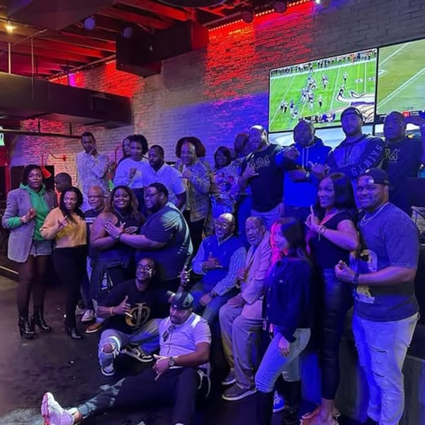 Group of people posing in a bar-&-grill with red and blue lighting and a football game on TV.