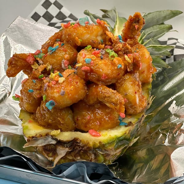 Sweet and sour shrimp with colorful cereal bits, served in a pineapple half on foil.