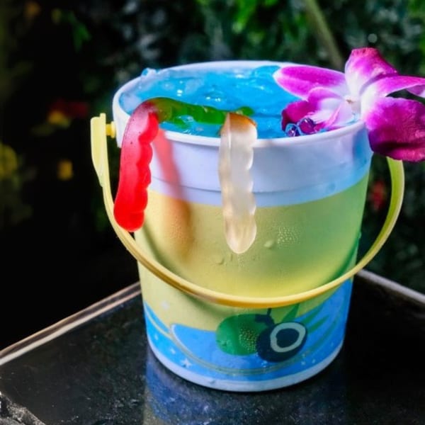 A colorful Cali Kitchen and Bar cocktail in a sand bucket with gummy worms and an orchid.